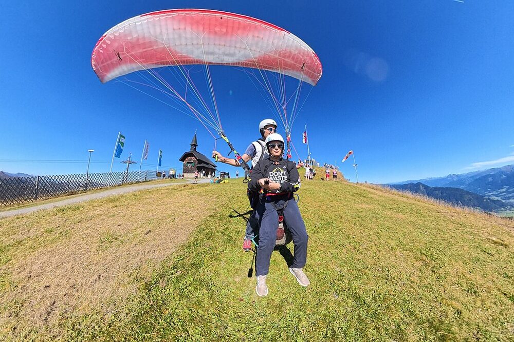 A tandem paraglider taking flight over green hills
